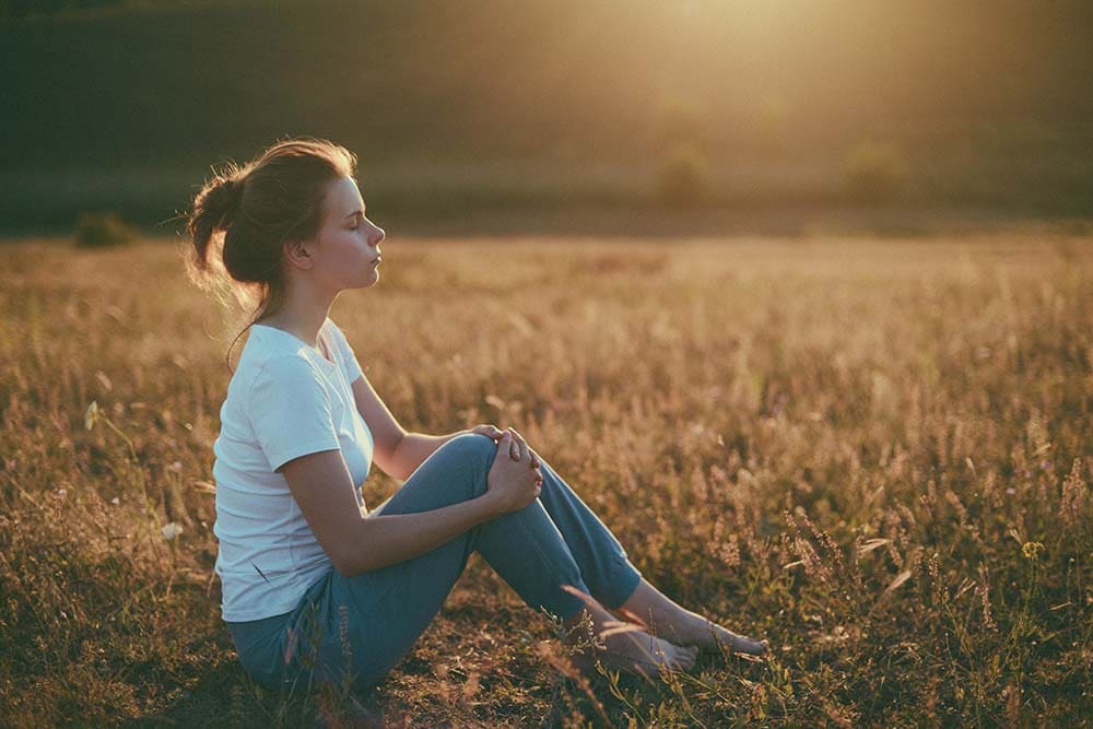 woman meditating in grassy field